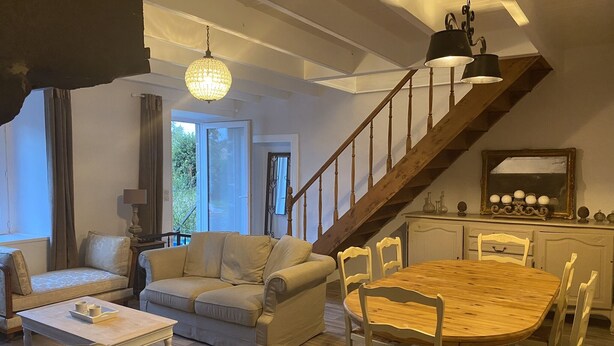 A spacious living area with a wooden staircase, a dining table with chairs, and a chandelier.