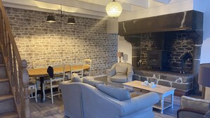 A cozy living room with a stone wall, a fireplace, a dining table with chairs, a sofa, and a staircase.