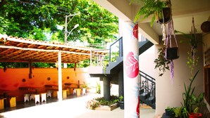 Un espace extérieur aménagé en terrasse, avec des tables et des bancs en bois, entouré de plantes en pot et de jardinières suspendues.