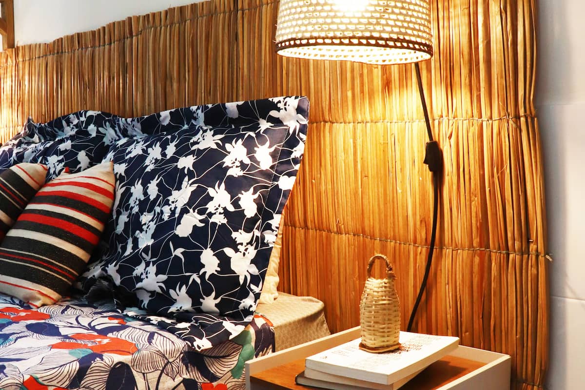 A bed with a floral bedspread, a bedside lamp, and a small table with a book and a lantern.