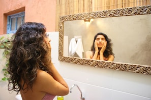 A bathroom with a mirror, sink, and a decorative wall panel. - Santo Hostel (Porto Seguro)