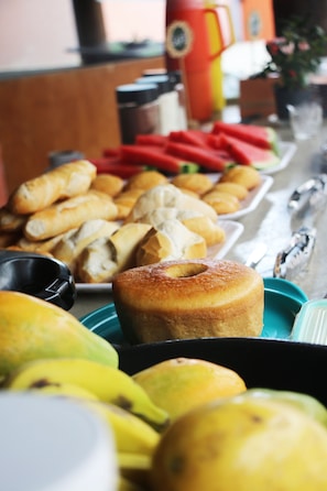 A buffet table with various food items including pastries, fruits, and vegetables. - Santo Hostel (Porto Seguro)