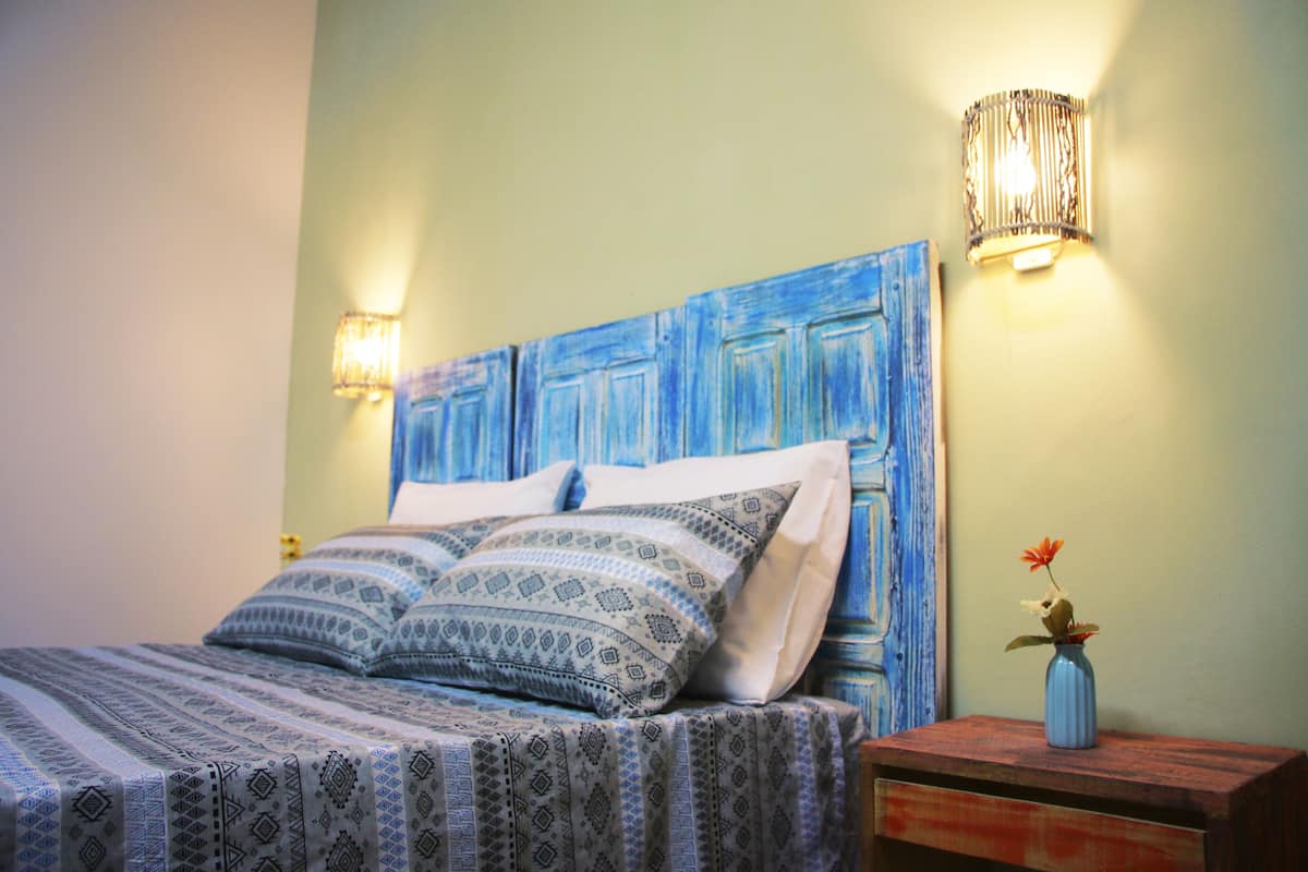 A bed with patterned bedding, a wooden headboard, and a nightstand with a vase of flowers.