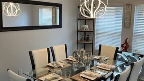 A dining area with a glass table, black chairs, and a modern pendant light. - Modern 5 Bedroom, 3 Full bathroom, + PlayStation. (Montgomery County)