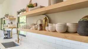 Uma cozinha com azulejos brancos, uma torneira dourada e prateleiras com utensílios de cozinha e plantas.