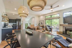 Une cuisine moderne avec des meubles de couleur sombre, un coin repas doté d’une longue table et un espace salon confortable avec une cheminée.