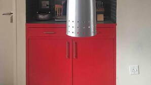 Una cocina con armarios rojos, una lámpara colgante de acero inoxidable y una pizarra en la pared.