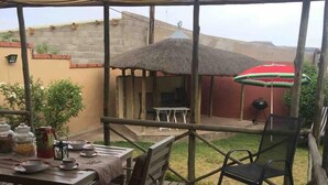 Una terraza de madera con mesa y sillas, una parrilla y un área cubierta con toldo a rayas.