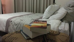 Una habitación de hotel con una cama, una mesita de noche con libros y una cortina.