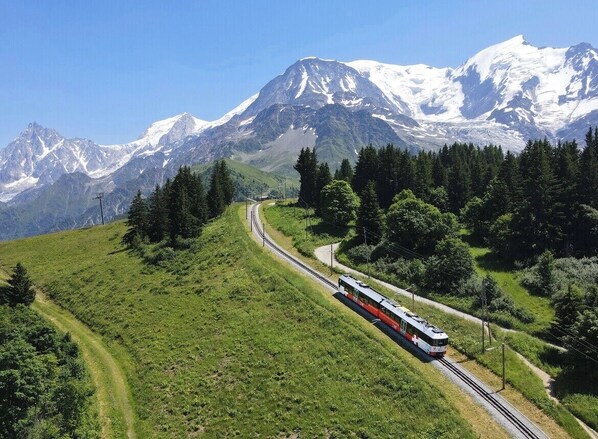A train on a mountain track with snow-capped peaks in the background.