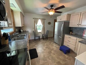 A compact kitchen with a refrigerator, microwave, and sink. There are two chairs and a small blue stool. - PSU Spacious Home. Free Parking, WiFi, Back Yard. (Pleasant Gap)
