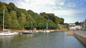 Um rio calmo com barcos atracados, rodeado por vegetação exuberante e uma pequena cidade ao fundo.