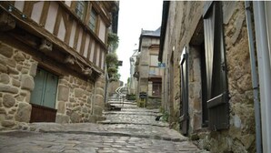 Uma rua de paralelepípedos estreita, ladeada por edifícios de pedra com estrutura de madeira, que leva a uma escadaria.