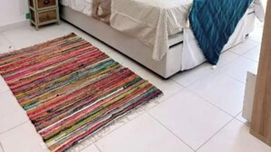 Um quarto com uma cama, um tapete listrado e colorido, uma mesa de cabeceira, uma luminária na parede e um quadro.