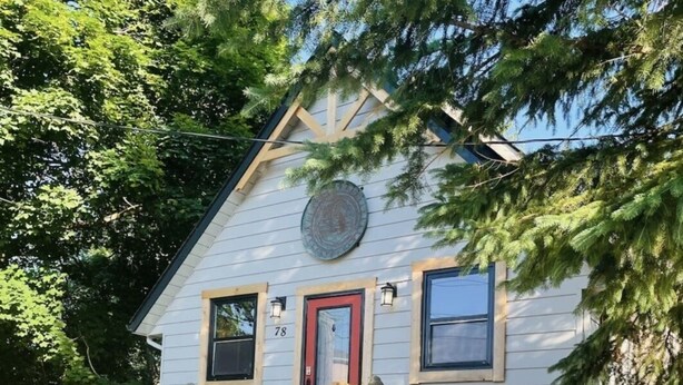 Une maison à deux étages avec une porte rouge, un petit porche et un escalier menant à l’entrée.