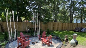 Une terrasse circulaire agrémentée de chaises Adirondack rouges, d’un foyer en pierre et d’un abreuvoir décoratif pour les oiseaux.