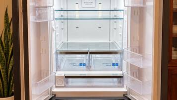 Ein offener Kühlschrank mit übersichtlichen Ablagefächern, einer Bedienblende und einer Pflanze daneben.