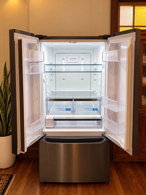 Ein offener Kühlschrank mit übersichtlichen Ablagefächern, einer Bedienblende und einer Pflanze daneben.