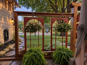 Una pérgola de madera con dos cestas de flores y una planta de helecho al frente.