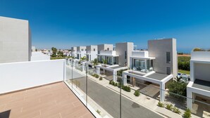 Un complesso residenziale moderno con edifici bianchi, un balcone con ringhiera in vetro e una vista aperta sul mare.