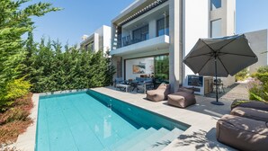 Un edificio moderno su due piani con piscina, area salotto esterna e un ombrellone grande.