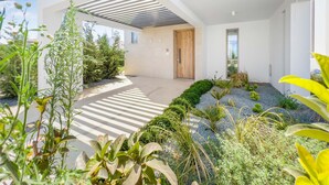 A modern building with a minimalist design, featuring a flat roof, large windows, and a well-maintained garden area with various plants and a gravel pathway.