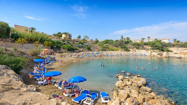 A beach with clear blue water, sun loungers, and umbrellas.