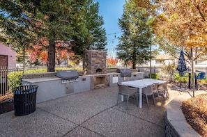 An outdoor patio with a stone barbecue, seating, and a trash can. - Lovely 1-bedroom Apartment In Great Location. (Roseville)