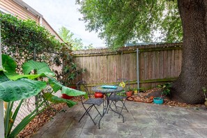 A patio with a round table and chairs, surrounded by potted plants and a wooden fence.