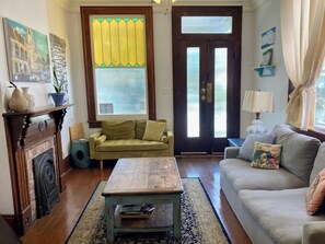 A living room with a fireplace, a green sofa, a wooden coffee table, and a large window with curtains.