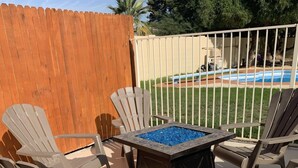 A patio with Adirondack chairs, a fire pit, and a view of a pool. - Your Oasis Retreat: Pool, style, comfort, relaxation (Phoenix)