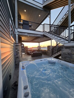 A hot tub area with a stone wall and a balcony overlooking a sunset. -  Suite A: New pool and hot tub for 2026! Relax & Unwind, Sleeps 18 (Ludington)