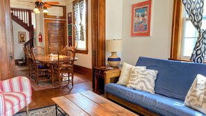 A living room with a wooden dining table, blue sofa, patterned rug, and a staircase leading to another room. - Half Okra Inn — Lovely, Historic, Streetcar in Sight, Restaurants & Bars Nearby (New Orleans)