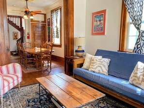 Un soggiorno con tavolo da pranzo in legno, divano blu, tappeto decorato e una scala che conduce a un'altra stanza.