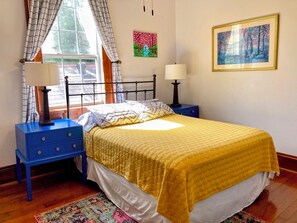 A bedroom with a bed, two bedside tables, a window with curtains, and two wall-mounted lamps.