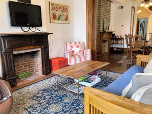 A living room with a fireplace, a television mounted above it, a patterned rug, a wooden coffee table, and a striped armchair.
