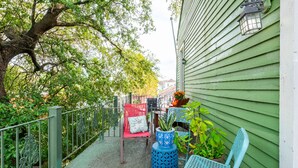 A narrow outdoor pathway with a metal railing, a blue chair, a red chair, and potted plants. - Half Okra Inn — Lovely, Historic, Streetcar in Sight, Restaurants & Bars Nearby (New Orleans)