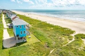 A coastal property with a prominent blue house, a sandy beach, and a clear view of the ocean.