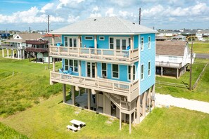 A two-story house with a balcony on the upper floor, a covered front porch, and a small front yard. - Beachfront Beauty w/ 2 King Suites, 2 Covered Decks, Panoramic Gulf Views 24/7 (Galveston)