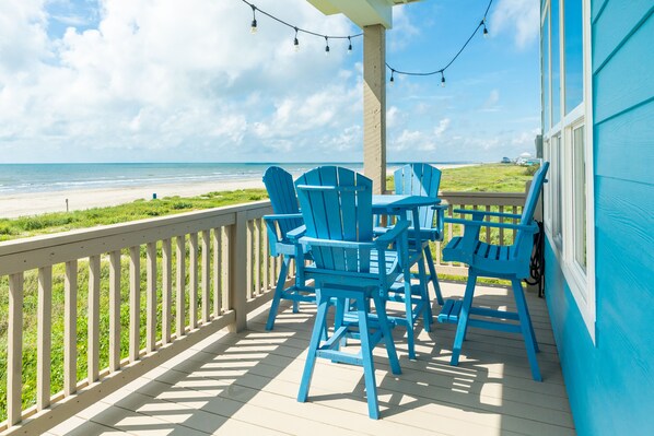 A covered deck with blue Adirondack chairs and a table, overlooking a beach. - Beachfront Beauty w/ 2 King Suites, 2 Covered Decks, Panoramic Gulf Views 24/7 (Galveston)