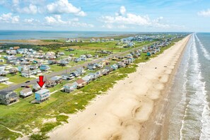 A coastal town with a long beachfront, houses along the road, and a visible road intersection with a red arrow. - Beachfront Beauty w/ 2 King Suites, 2 Covered Decks, Panoramic Gulf Views 24/7 (Galveston)