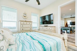 A bedroom with a bed, dresser, TV, and a view into the living area. - Beachfront Beauty w/ 2 King Suites, 2 Covered Decks, Panoramic Gulf Views 24/7 (Galveston)