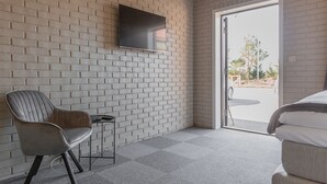 A modern room with a brick wall, a flat-screen TV mounted above a chair, and a bed with a view through a glass door. - Aksdal Inn Motell (Tysvaer)