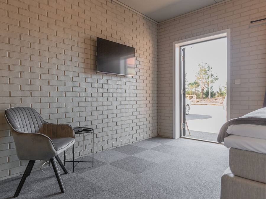 A modern room with a brick wall, a flat-screen TV mounted above a chair, and a bed with a view through a glass door.