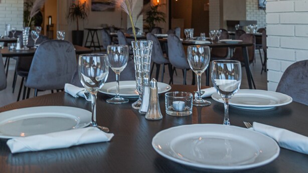 A restaurant with round tables set for dining, clear glass pendant lights, and a brick wall. - Aksdal Inn Motell (Tysvaer)