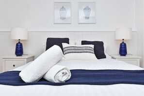 A neatly made bed with white and navy bedding, two pillows, and a rolled white towel.