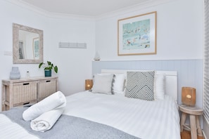 A bedroom with a bed, bedside tables, a dresser, a mirror, a painting, and a potted plant.