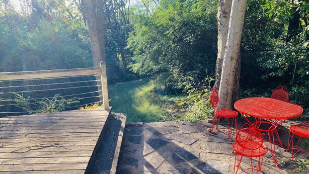 A wooden deck with a metal railing, a stone pathway, and red metal chairs and tables.