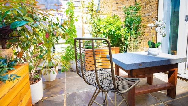Un patio con una silla de metal, una mesa y plantas en macetas.