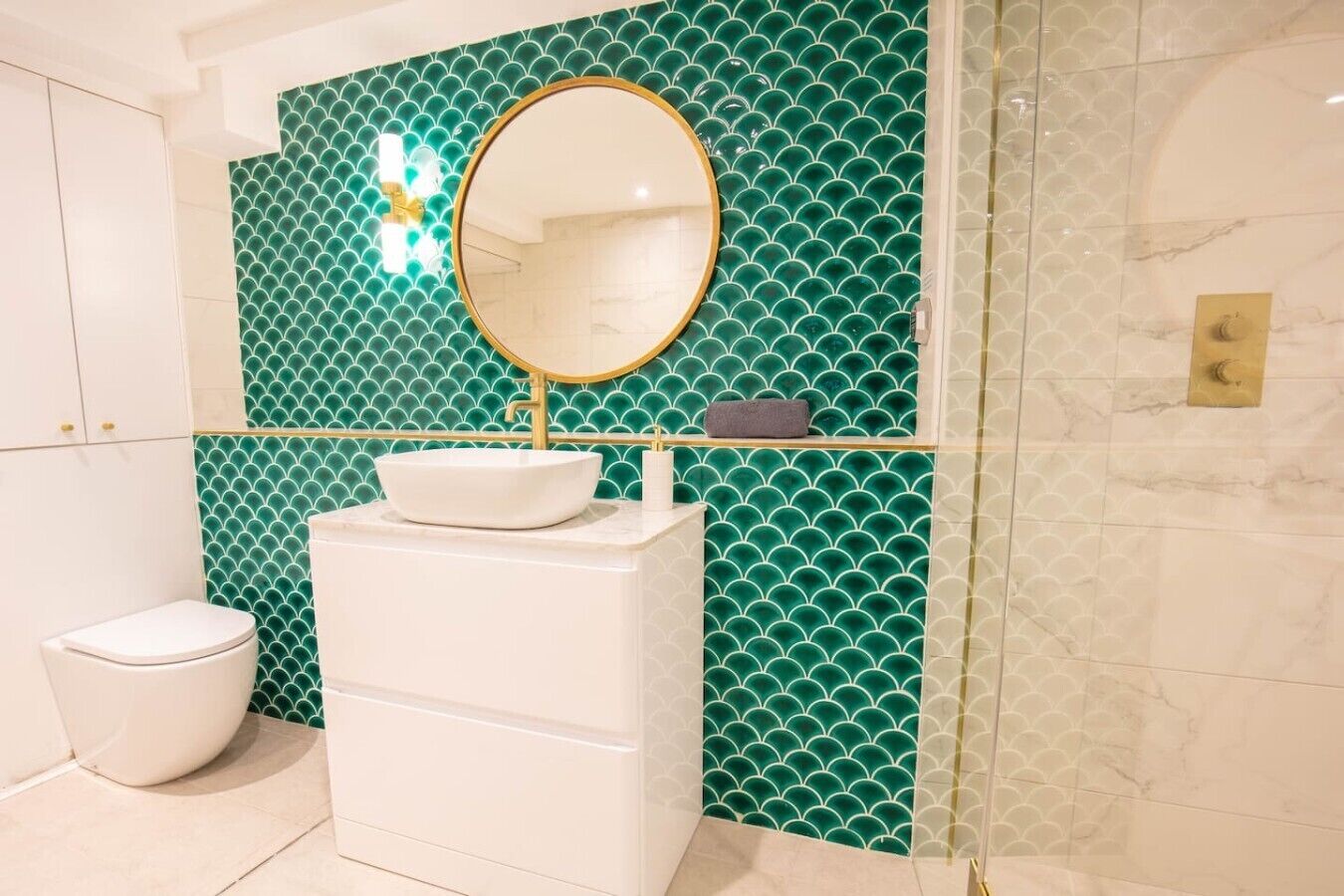 Une salle de bain avec un lavabo blanc, un miroir rond et des toilettes.